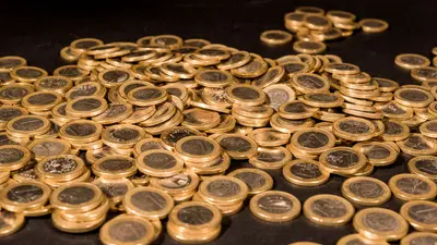 Une grande quantité de pièces de monnaie dorées éparpillées sur une surface sombre.