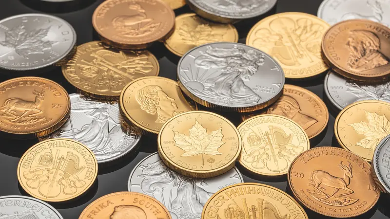 Un ensemble de pièces d'or et d'argent d'investissement disposées sur une surface sombre.