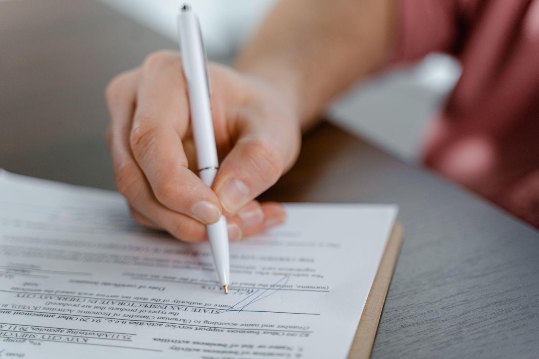 Une main tenant un stylo blanc et signant un document administratif posé sur une table.